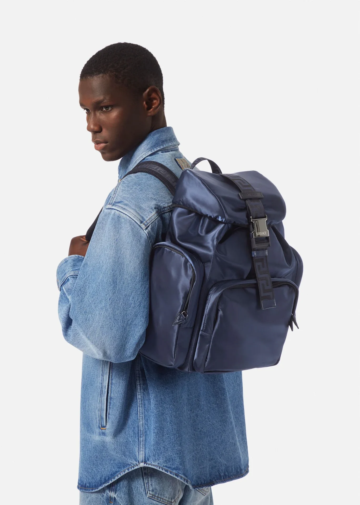 A man in blue jacket and jeans holding a backpack.